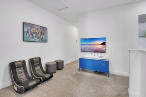 A room with a flat-screen TV, two reclining chairs, a blue cabinet, and a framed picture on the wall. - 4BR Family Townhome, pool, resort & Splash (Davenport)