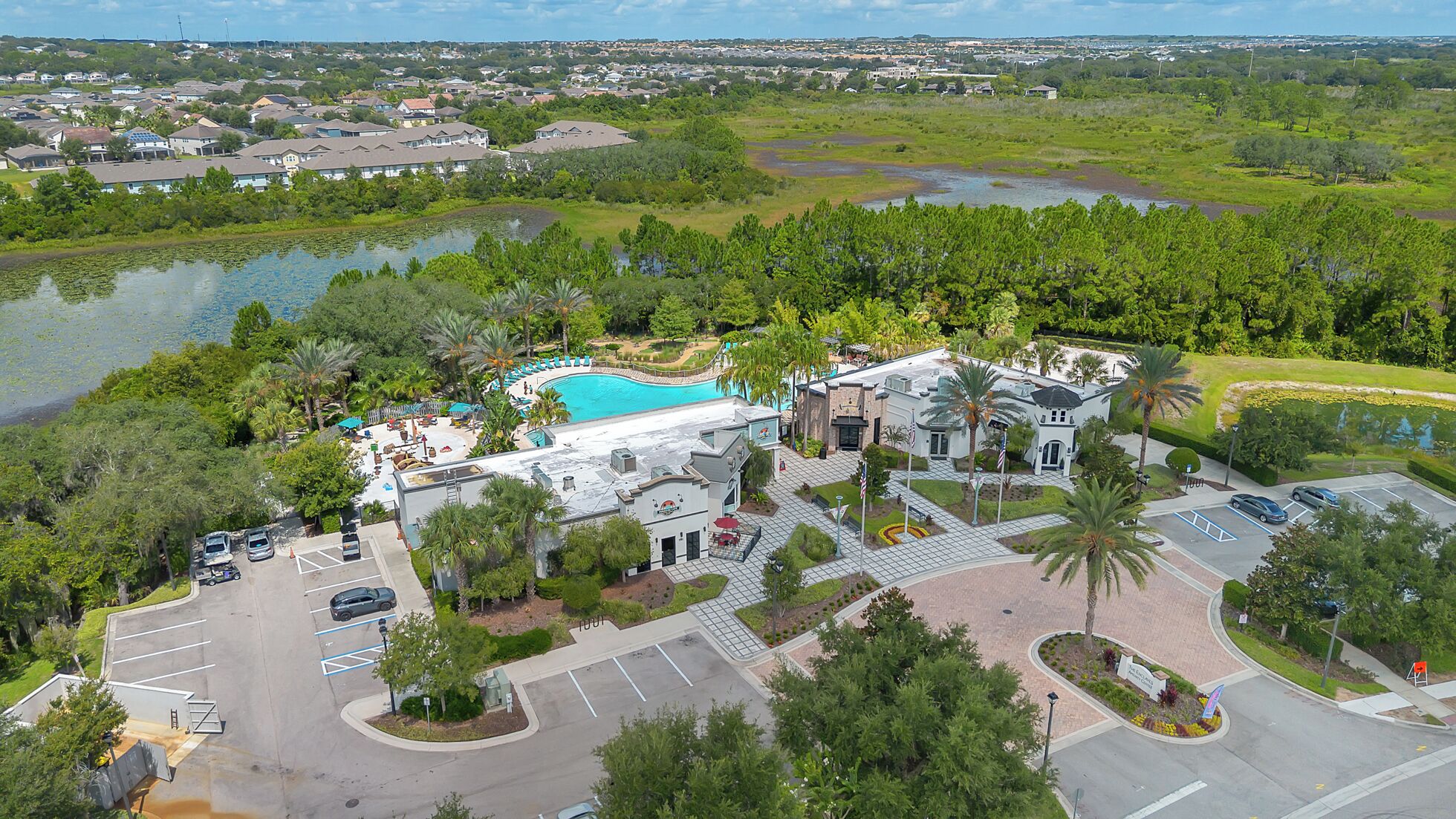 An aerial view of a resort with a swimming pool, parking area, and surrounding greenery.