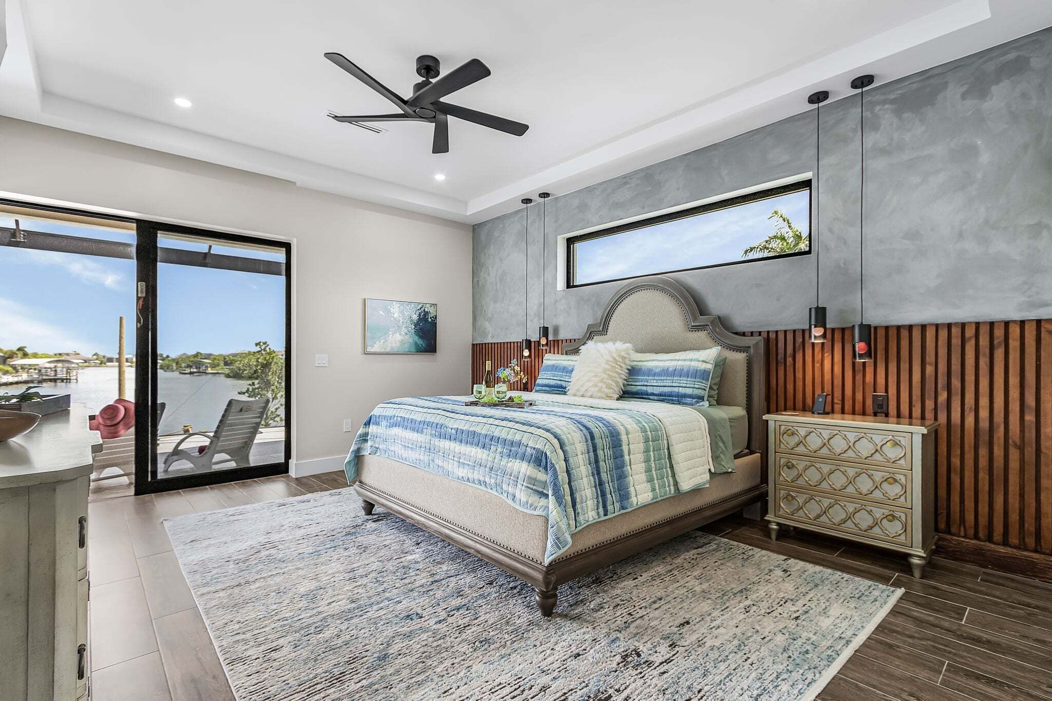 A bedroom with a large bed, a ceiling fan, a window with a view, and a nightstand.