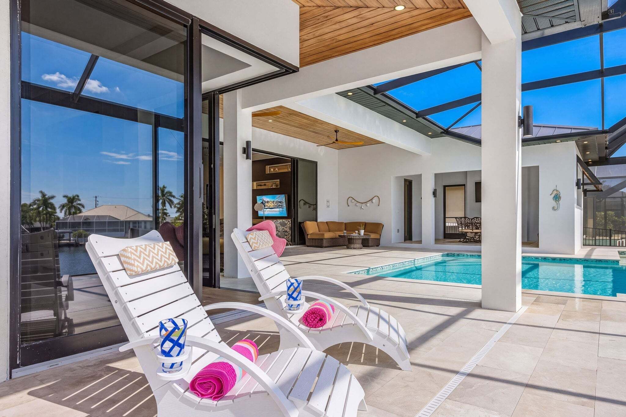 A modern outdoor pool area with two lounge chairs, a television, and a dining area.