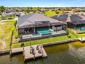 A residential property with a swimming pool, a covered patio, and a dock extending into a body of water. - Pool and Spa, Dock, Kayaks & Outdoor Kitchen - Coastal Elegance Retreat - Roelens (Cape Coral)