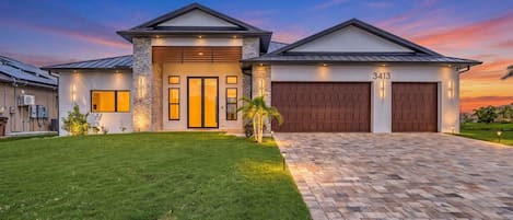A modern two-story house with a driveway leading to a garage, a well-maintained lawn, and a clear sky.