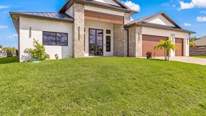A modern two-story house with a garage, a well-maintained lawn, and a clear blue sky.