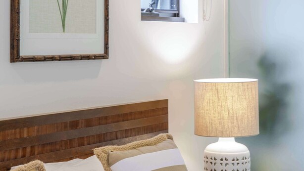 A neatly made bed with striped pillows and a textured throw, a bedside lamp, and a framed botanical print on the wall. - SeaEden @ The Temple Studio Spa Apartment (Craiglie)