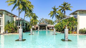 A resort pool with clear water, surrounded by palm trees and modern buildings. - SeaEden @ The Temple Studio Spa Apartment (Craiglie)