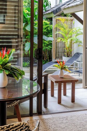 Une terrasse fermée par des baies vitrées, avec une table ronde, deux chaises et des plantes en pot.