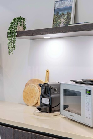 Eine Küchenarbeitsplatte mit einer Kaffeemaschine, einer Mikrowelle, einem Holzschneidebrett und einer hängenden Pflanze.