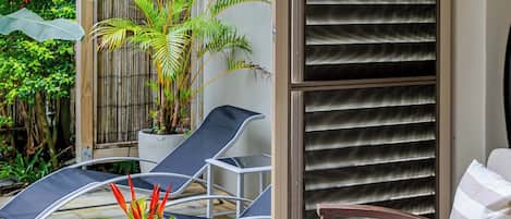 A patio area with a wooden table, a chair, a potted plant, and a sliding glass door.