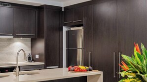 A modern kitchen with dark cabinetry, a stainless steel refrigerator, and a dining area with a wooden table and chairs. - SeaEden @ The Temple 3 Bedroom with Private Pool (Craiglie)