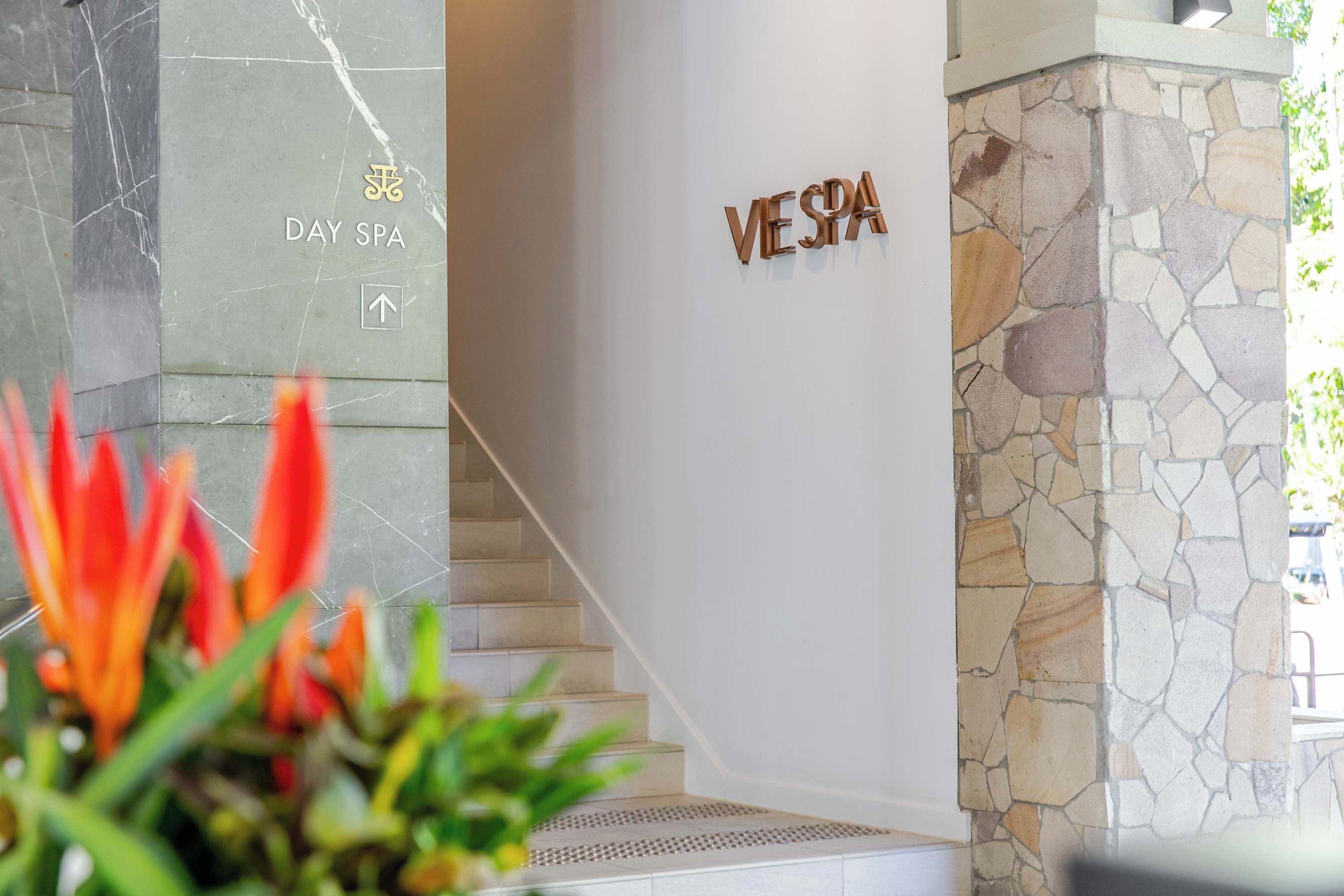 Zona de recepción con pared de mármol, pared de piedra y una escalera. Se muestra la palabra 'VESPA' de manera destacada.