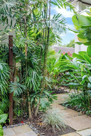 A lush garden with various tropical plants, a wooden pergola, and a stone pathway. - SeaEden @ The Temple 3 Bedroom with Private Pool (Craiglie)