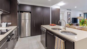 A modern kitchen with dark cabinetry, stainless steel appliances, a central island with a sink, and a dining area with a table and chairs. - SeaEden @ The Temple 3 Bedroom with Private Pool (Craiglie)