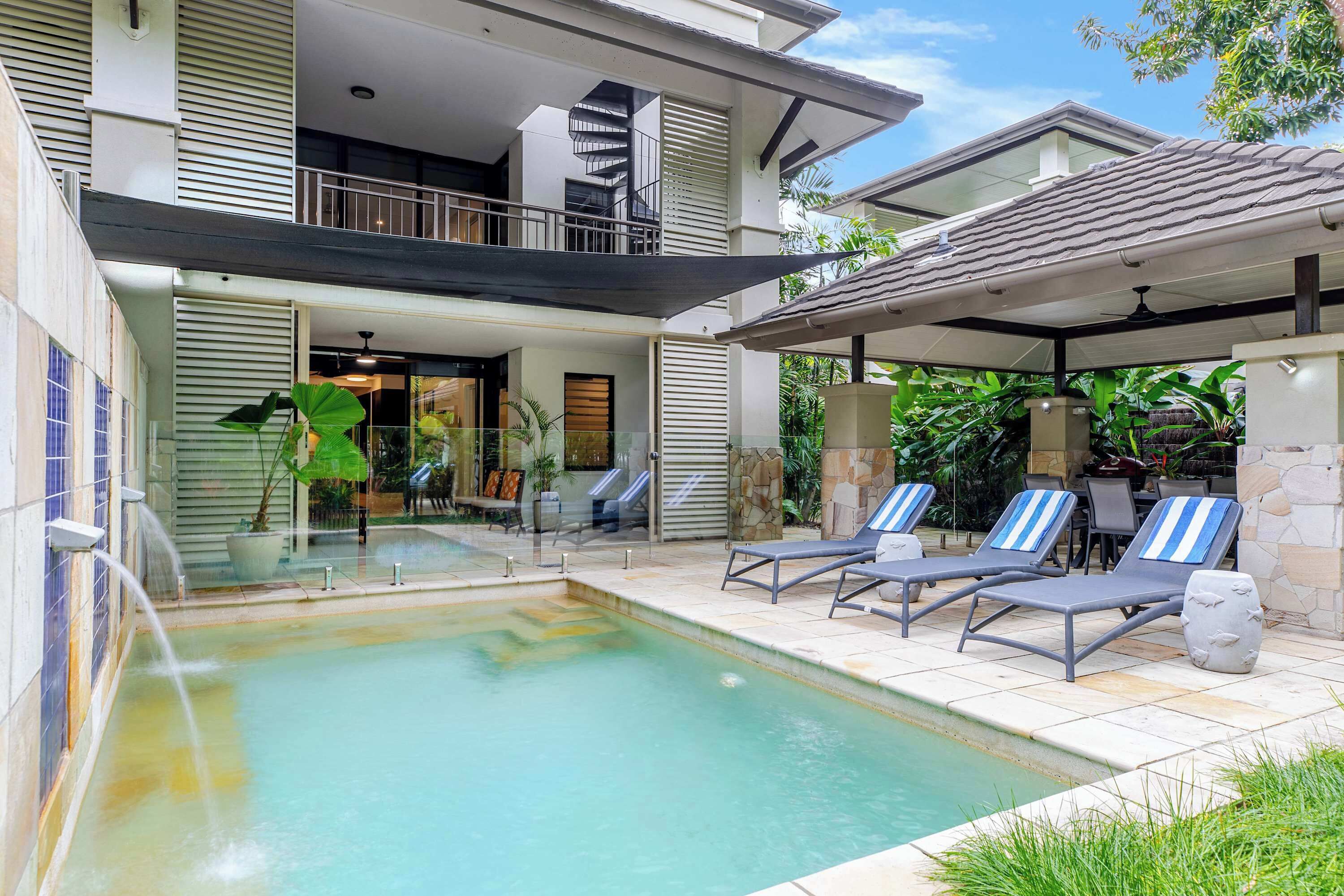 A modern two-story building with a swimming pool, outdoor seating, and a covered patio area.