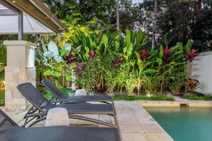 Uma área junto à piscina com espreguiçadeiras e diversas plantas tropicais.