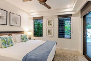 A bedroom with a bed, a ceiling fan, framed artwork, and a view through the window. - SeaEden @ The Temple 2 Bedroom with Private Pool (Craiglie)