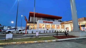 A Popeyes restaurant with a modern design, a parking lot, and a nearby statue.