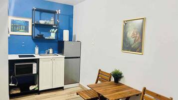 Une cuisine de taille réduite avec un mur d’accent bleu, un réfrigérateur, un four à micro-ondes et une table à manger avec des chaises.