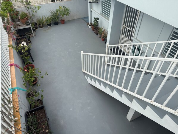 A rooftop terrace with potted plants, a white railing, and a grey floor.