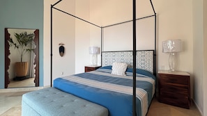 Ein Schlafzimmer mit Himmelbett, Nachttisch mit Lampe, Wanddeko und Zimmerpflanze.