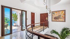 Een modern interieur met een glazen deur naar een balkon, een houten trap en een decoratief wandobject.