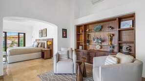 A spacious living area with a large bed, a sofa, and a coffee table. There is a wooden cabinet with decorative items and a view of the outdoors. - Stunning 5BR Oceanview Villa in Conchas Chinas (Puerto Vallarta)