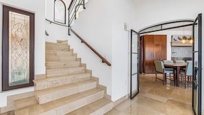 Eine Holzhandlauf-Treppe führt zu einem Essbereich, im Hintergrund ist eine Küche zu sehen.