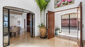 A modern interior with a curved glass door leading to a dining area, a large potted plant, and a decorative metal gate. - Stunning 5BR Oceanview Villa in Conchas Chinas (Puerto Vallarta)