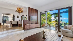 A modern living room with a large TV, wooden panel wall, and a view of the sea. - Stunning 5BR Oceanview Villa in Conchas Chinas (Puerto Vallarta)