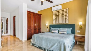 Een slaapkamer met een bed, een houten kledingkast, wandairconditioning en een plafondventilator.