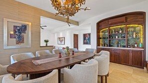 A spacious dining area with a long wooden table surrounded by upholstered chairs, a decorative chandelier, and a wine display cabinet. - Stunning 5BR Oceanview Villa in Conchas Chinas (Puerto Vallarta)