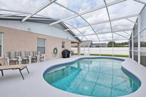 A covered outdoor swimming pool with lounge chairs and a barbecue area. - Best Value Near Disney! Private Pool, BBQ, Fenced Yard & Room for 8 (Kissimmee)