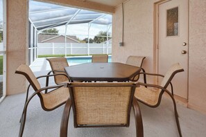 A covered patio with a table and chairs, a pool in the background, and a door with a small window. - Best Value Near Disney! Private Pool, BBQ, Fenced Yard & Room for 8 (Kissimmee)