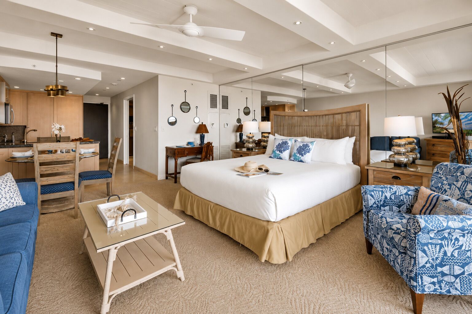 Une chambre d’hôtel moderne dotée d’un grand lit, d’un coin salon avec un canapé et un fauteuil, d’un petit bureau et d’une kitchenette.