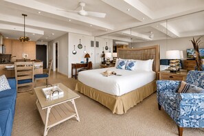 Ein modernes Hotelzimmer mit einem großen Bett, einer Sitzecke mit Sofa und Sessel, einem kleinen Schreibtisch und einer Küchenzeile.