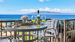 A table with a bottle and glasses on a balcony overlooking a beach and ocean. - Whaler 1261 Beautiful Studio Ocean View - Special introductory rates (Lahaina)