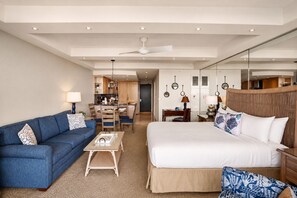 Ein Hotelzimmer mit einem Bett, einem Schlafsofa, einem Couchtisch, einem Schreibtisch und einer Küchenzeile im Hintergrund.