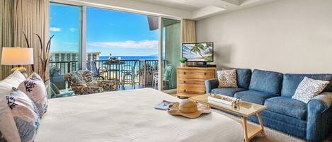 Ein Hotelzimmer mit einem großen Bett, einer Sitzecke, einem Fernseher und einem Balkon mit Meerblick.