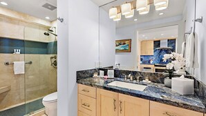 A modern bathroom with a glass-enclosed shower, a marble countertop, and a large mirror. - Whaler 1261 Beautiful Studio Ocean View - Special introductory rates (Lahaina)