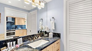 A modern bathroom with a large mirror, a sink with multiple faucets, and a countertop with toiletries. - Whaler 1261 Beautiful Studio Ocean View - Special introductory rates (Lahaina)