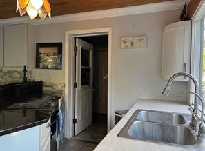 A compact kitchen with a black countertop, stainless steel sink, and a door leading to another room. - Charming 1-bedroom Guesthouse in Amazing Ozona Free Parking, Walk to Restaurants (Palm Harbor)