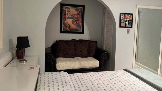 A bedroom with a bed, a nightstand, a lamp, a sofa, and a painting. - Charming 1-bedroom Guesthouse in Amazing Ozona Free Parking, Walk to Restaurants (Palm Harbor)