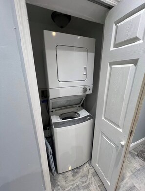 Ein kompakter Waschraum mit integriertem Waschmaschine und Trockner, einem kleinen Fenster und einer Tür zu einem weiteren Raum.