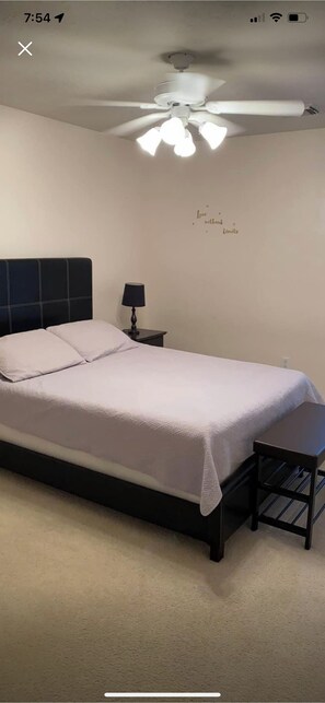 A bedroom with a bed, a nightstand, a lamp, a ceiling fan, and a wall with a decorative phrase. - 3-bedroom flat in Cypress ,second floor with independent entrance  (Cypress)