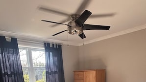 A bedroom with a bed, a ceiling fan, a wooden cabinet, and a window with curtains.