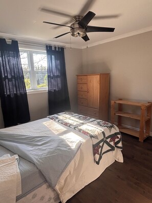 A bedroom with a bed, a ceiling fan, a wooden cabinet, and a window with curtains.
