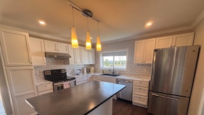 A modern kitchen with white cabinetry, a stainless steel refrigerator, and pendant lighting.
