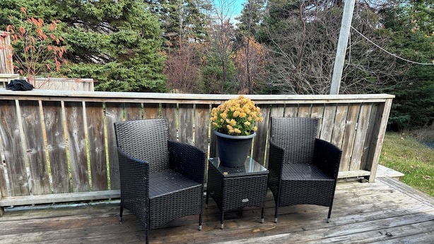 A wooden deck with two wicker chairs and a table, surrounded by a wooden fence and trees.