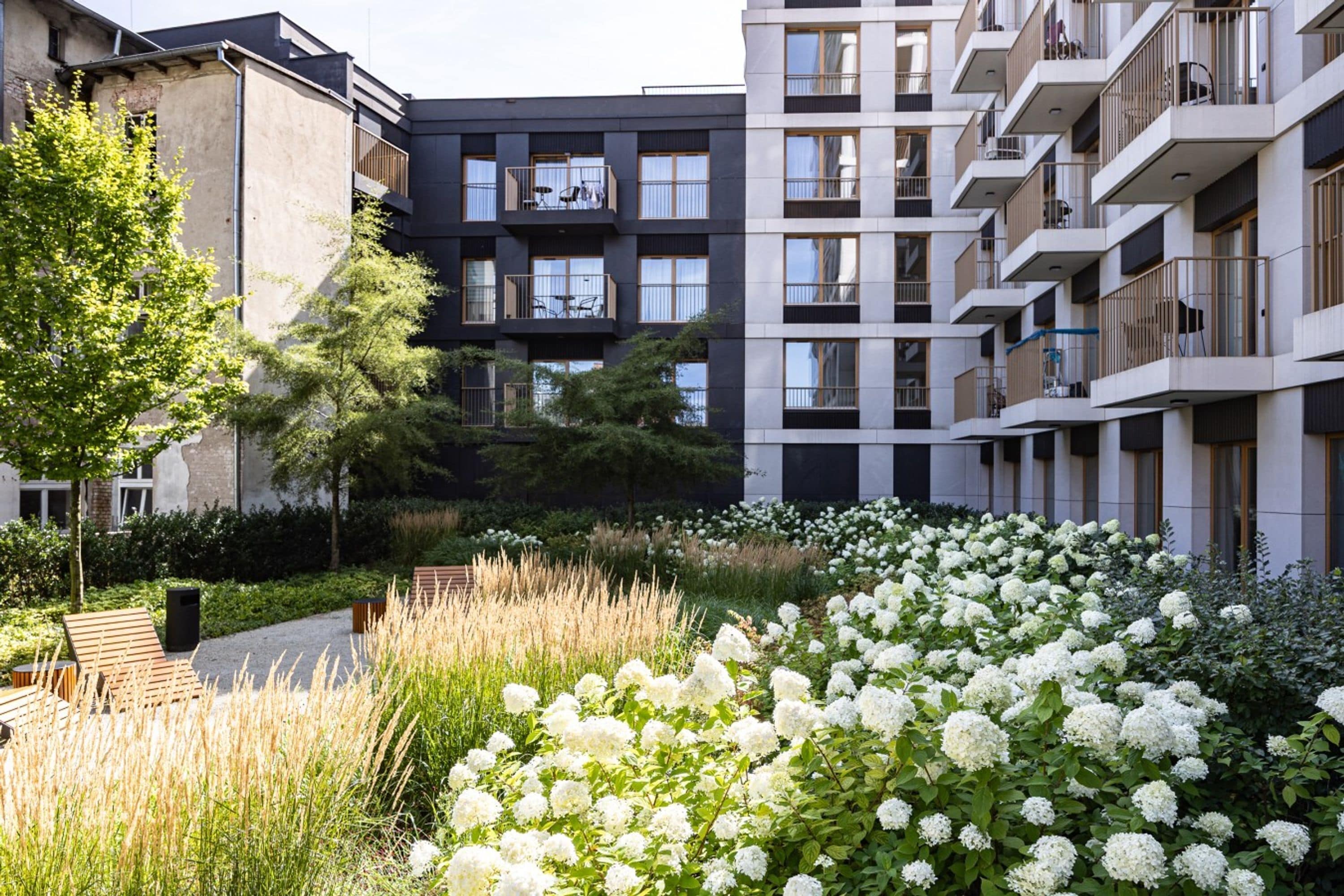 Un moderno edificio de apartamentos con balcones y un jardín lleno de flores blancas.