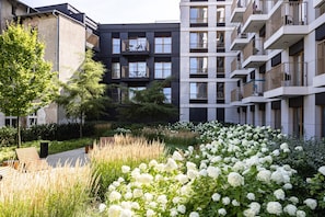 Un moderno edificio de apartamentos con balcones y un jardín lleno de flores blancas.