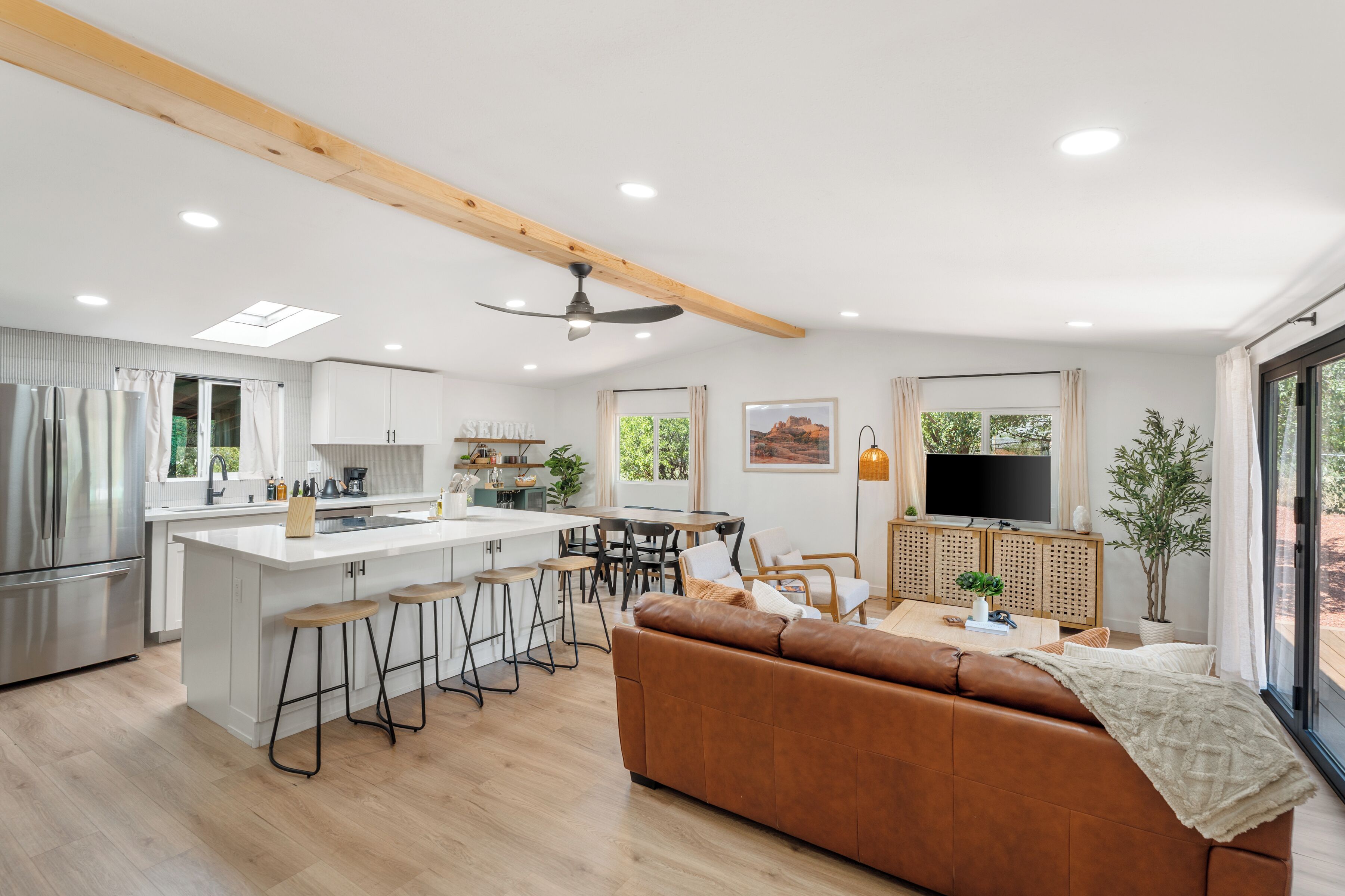 A modern kitchen with a central island, bar stools, a wooden ceiling, and a large window.